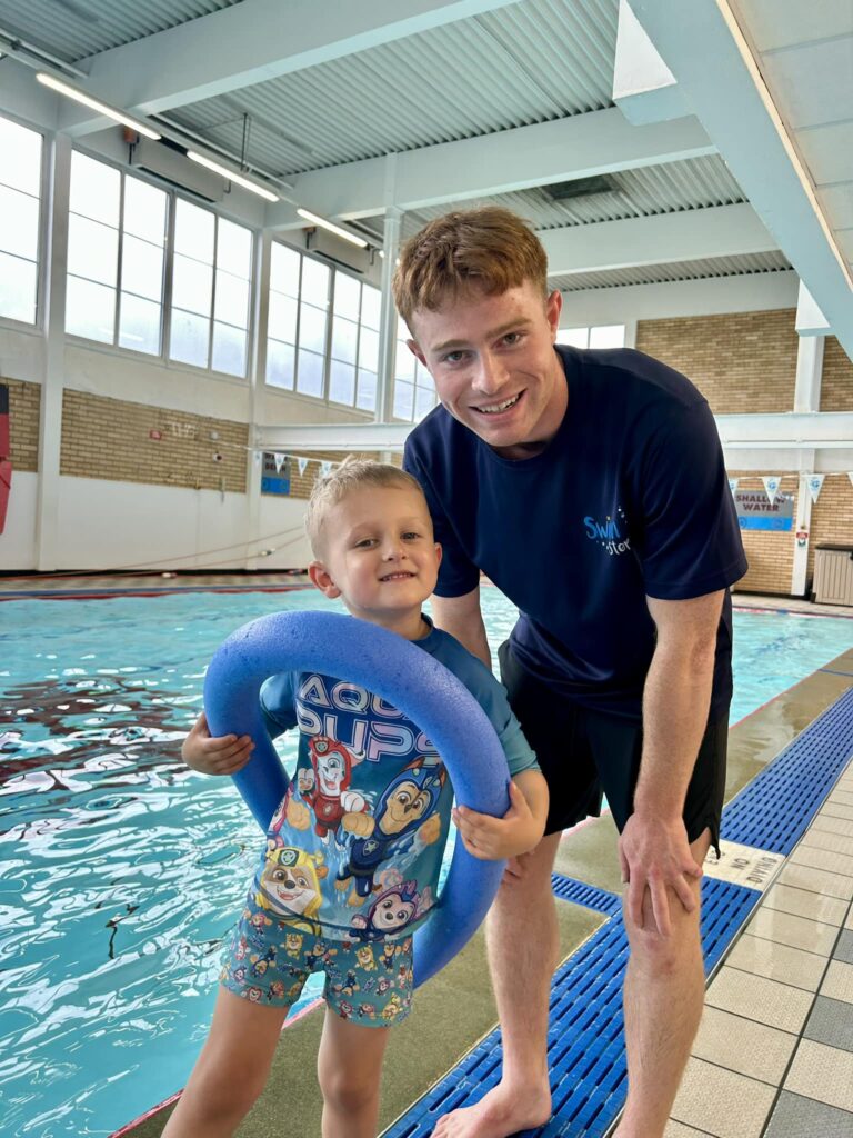 Swimming Instructor, part of Swim Steps Swimming Team, leaning in towards a happy child, both smiling at the camera, about to jump in the swimming pool